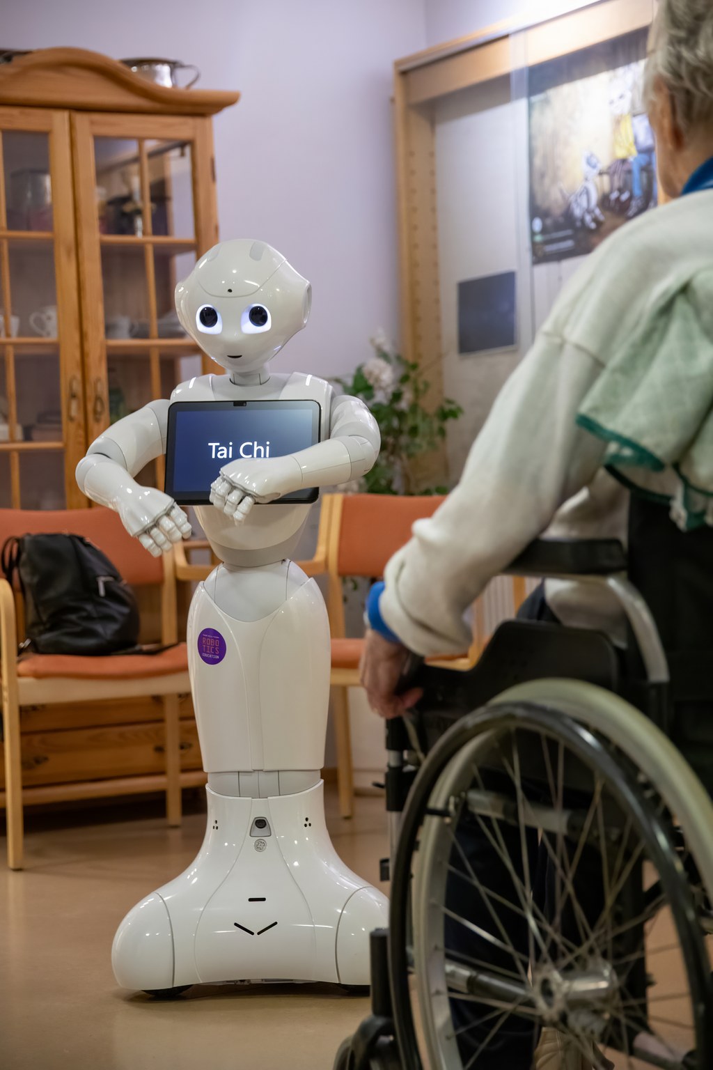 Pepper-robotti ohjaa jumppaa. Pepper muistuttaa jonkin verran ihmistä. Se seisoo, sillä on kädet, pää ja kasvot. Sen edustalla on pyörätuolissa istuva ihminen.