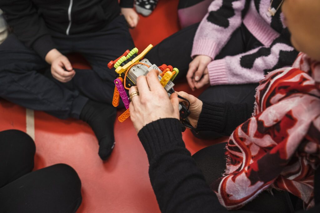 A plastic robot in the hands of an adult. Three children sitting around the adult.
