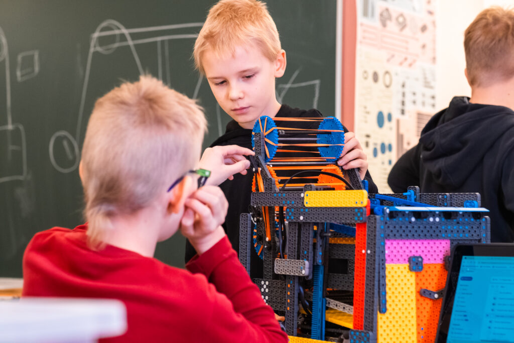 Kaksi poikaa robotin äärellä. Robotti on kirjava, moniosainen ja sillä hymyilevät kasvot.