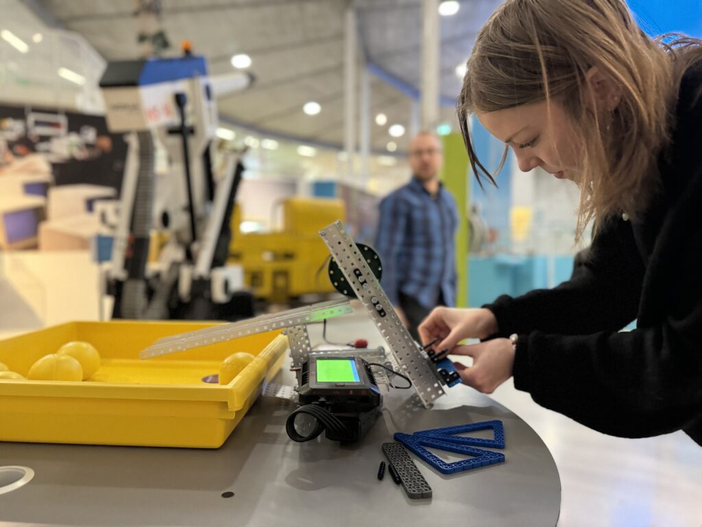 Robotiikkatyöpiste. Robotin ääreen on kumartunut nainen ja taustalla seisoo mies.
