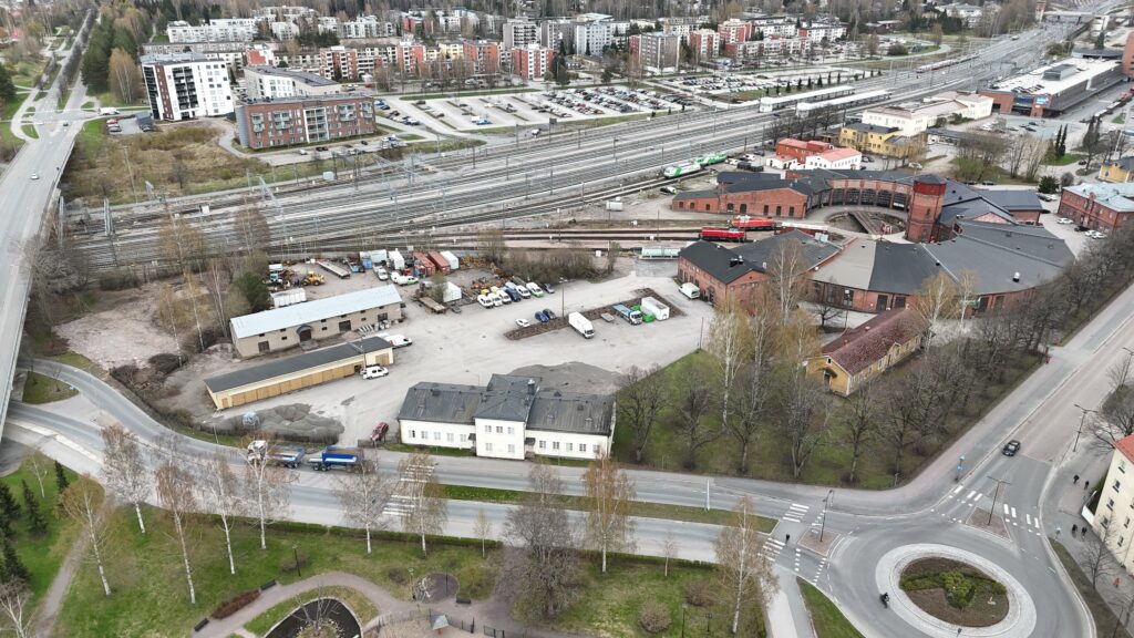 Ilmakuva, jossa näkyy useita erilaisia rakennuksia, kuten rautatieasema ja veturitallit. Kuvassa myös junaratoja ja useita katuja.