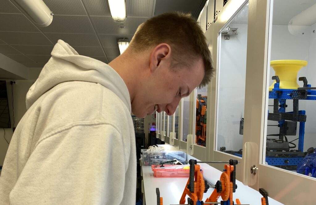 Nuori mies kumartuneena pöydän ääreen. Pöydällä on robotteja.
