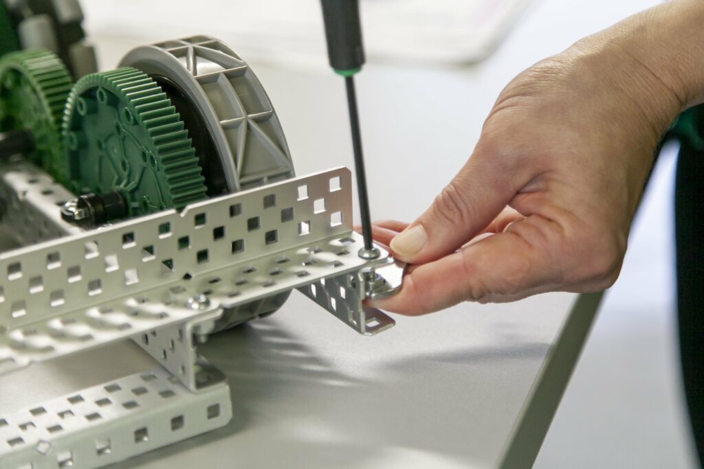 Ruuvimeisseli, jolla ruuvataan robotin ruuvia. Käsi tukee pitää kiinni robotista.