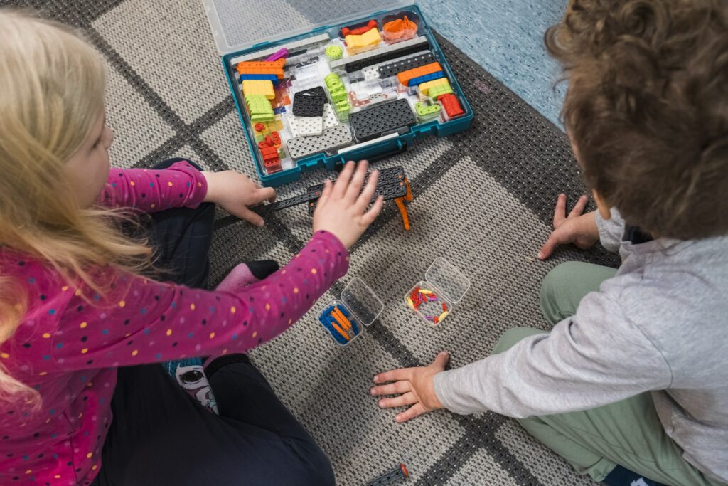 Kaksi pikkulasta lattialla värikkään tarvikelaatikon ääressä.