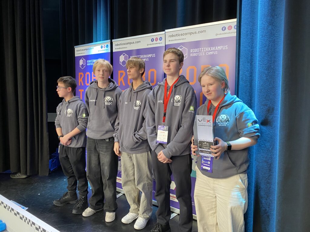 Neljä poikaa ja yksi tyttö ohjelmalavalla. Tytöllä on käsissään palkinto.