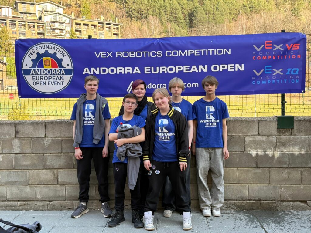 Viishenkinen joukkue ja valmentaja seisovat ulkona kisamainoslakanan edessä. Taustalla vuoristo.