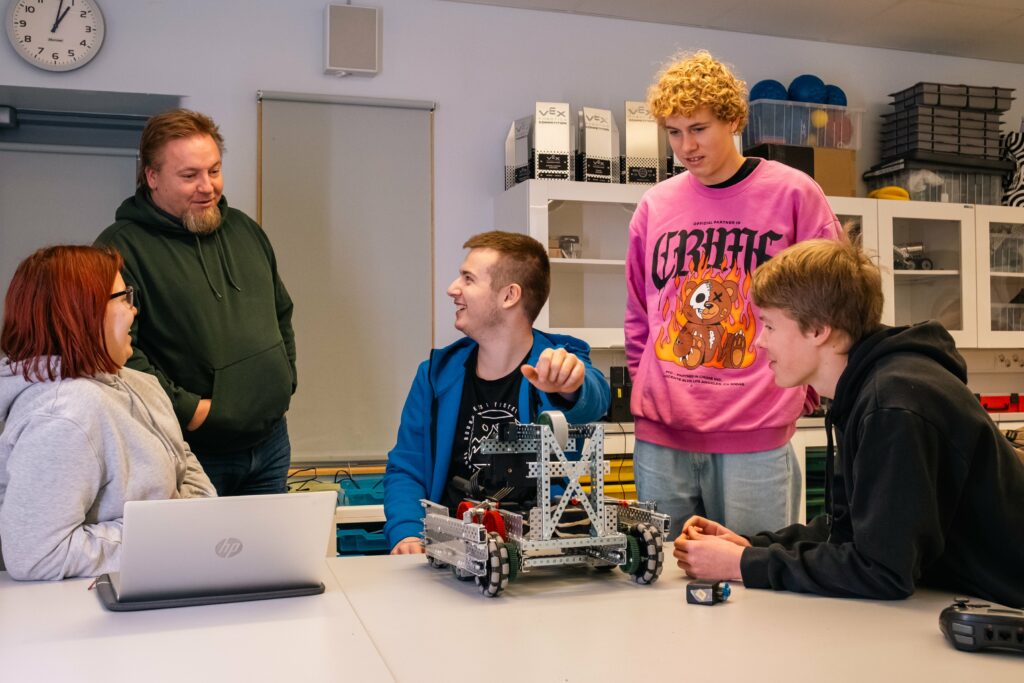 Lukiolaisia ja opettaja pöydän äärellä. Pöydällä on vex-robotti.