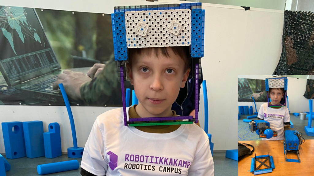 Poika, jolla on vex-osista tehty kypärä. Kuvassa sisällä pikkukuva, jossa on sama poika kypärä päässä ja robottikädet käsissä.
